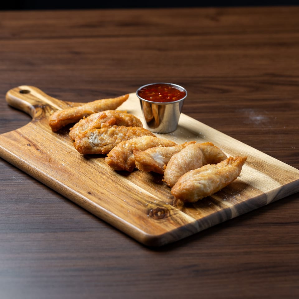Golden-fried chicken wings with a side of sweet chili dipping sauce on a wooden cutting board.