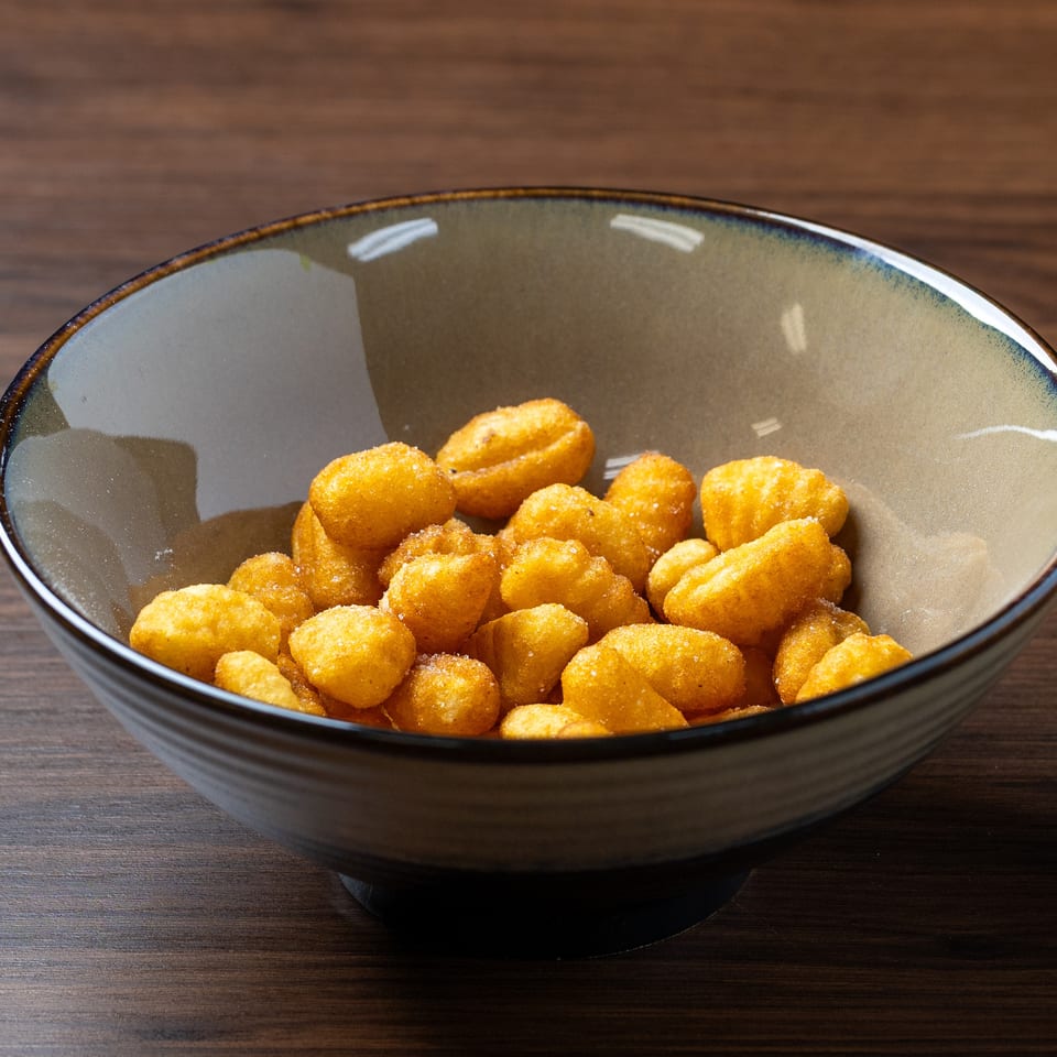 A bowl of golden-brown, crispy fried potato tots, lightly salted, on a dark wooden table.