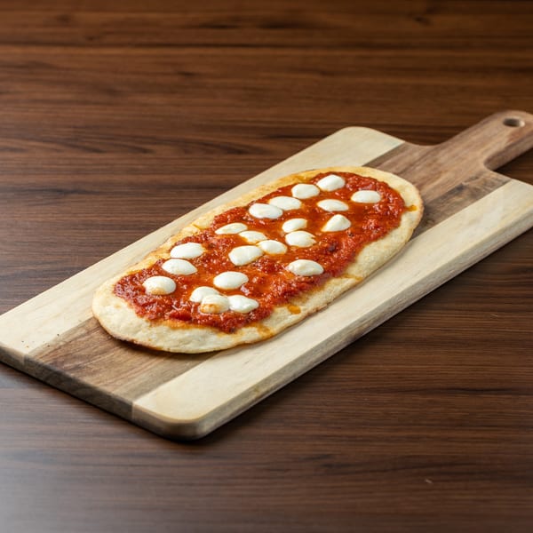 Flatbread pizza with tomato sauce and fresh mozzarella balls on a two-toned wooden cutting board.