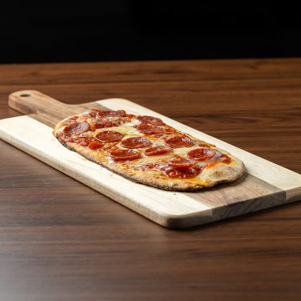 A rectangular pepperoni flatbread pizza with melted cheese and sauce on a wooden serving board.