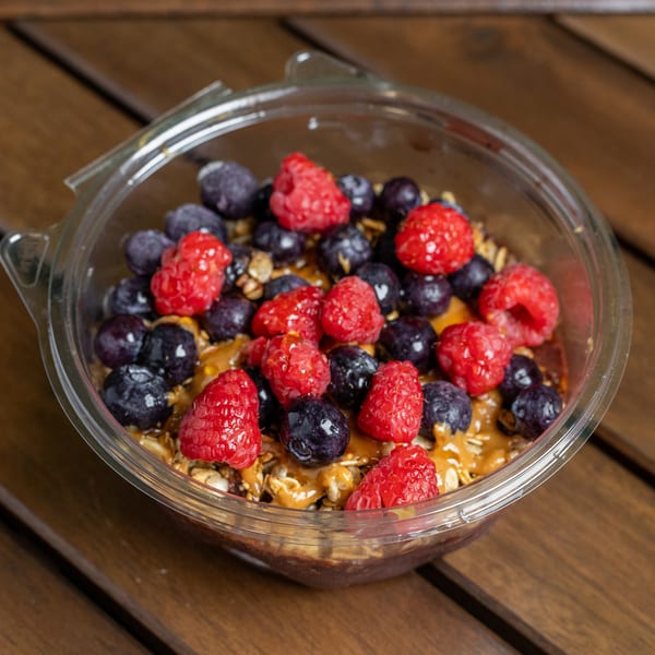 A clear plastic bowl filled with an acai bowl, topped with raspberries, blueberries, and granola.