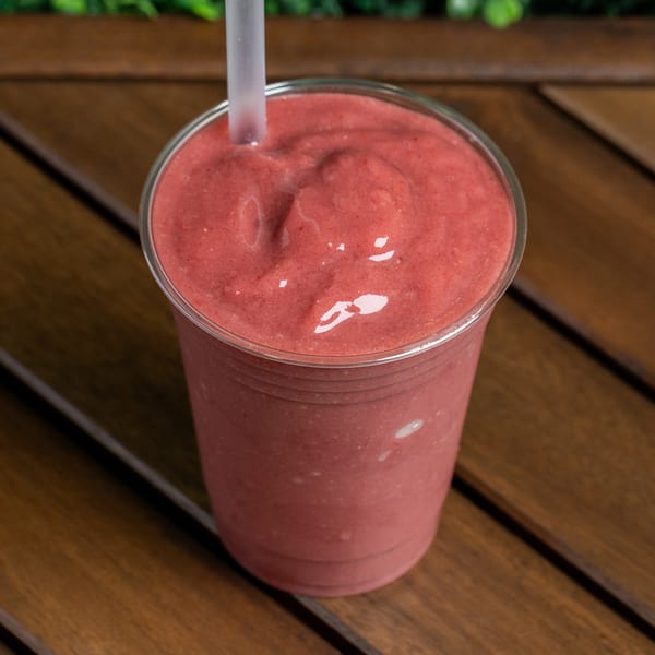 A vibrant pink strawberry smoothie with a straw in a clear cup on a wooden table.