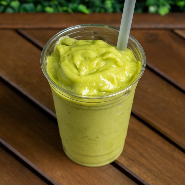 A vibrant green smoothie in a clear plastic cup with a straw, on a wooden table.